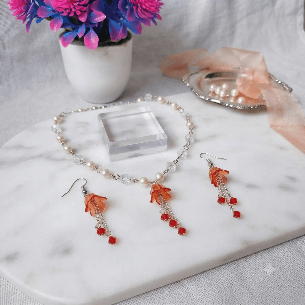 Handmade red floral necklace and matching earrings displayed with white, clear and red beads on a marble-style jewellery stand.