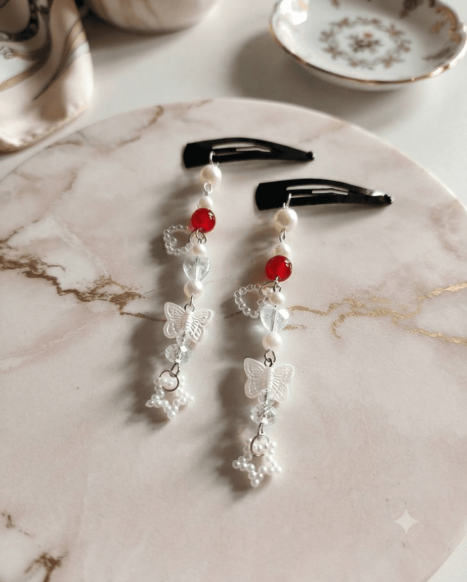 Pair of red and white beaded butterfly hair clips with long cascading charms displayed on a marble-style surface.