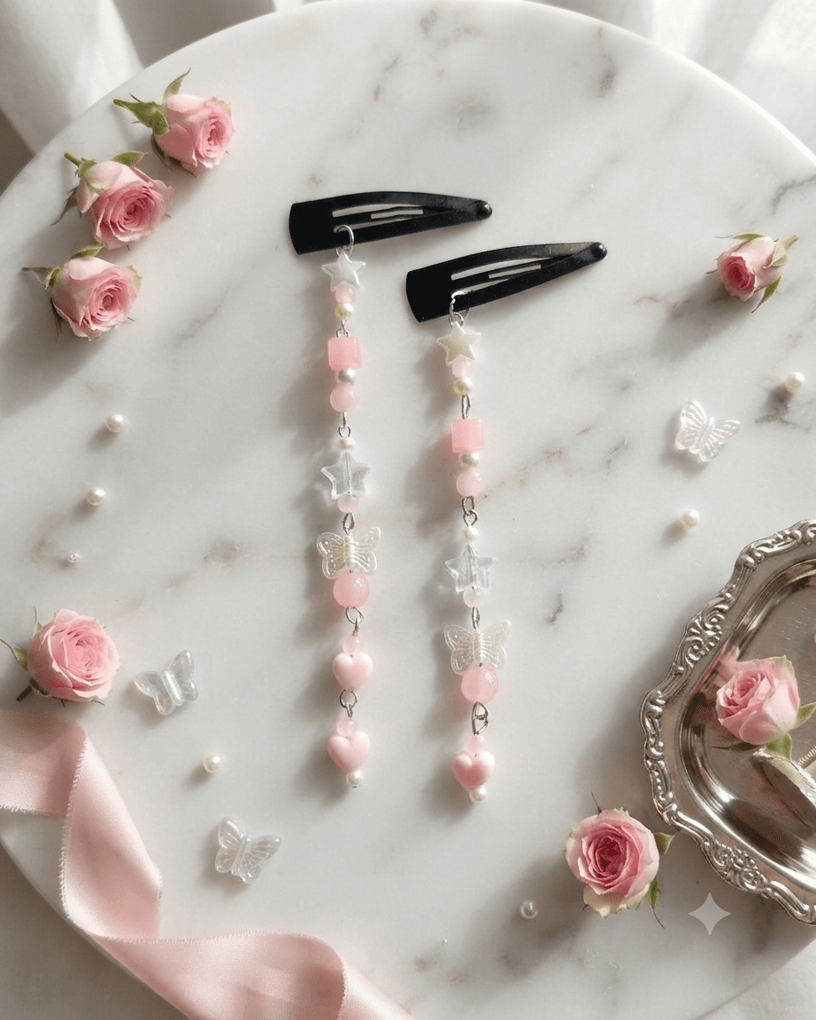 Pair of pastel pink and white beaded butterfly star hair clips with long decorative dangles displayed on a white marble-style surface.