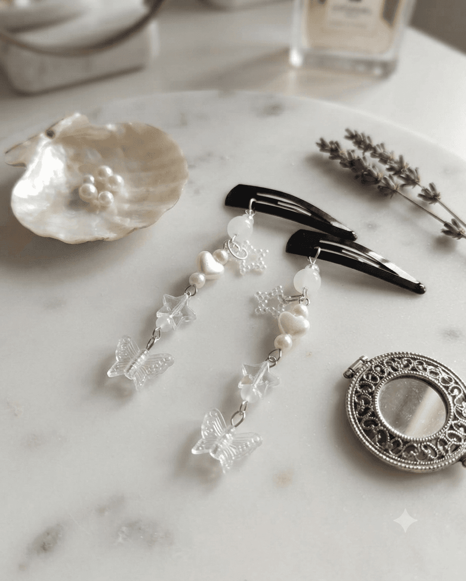 Pair of l white handmade butterfly hair clips with heart, star and cascading bead details displayed on a white surface.