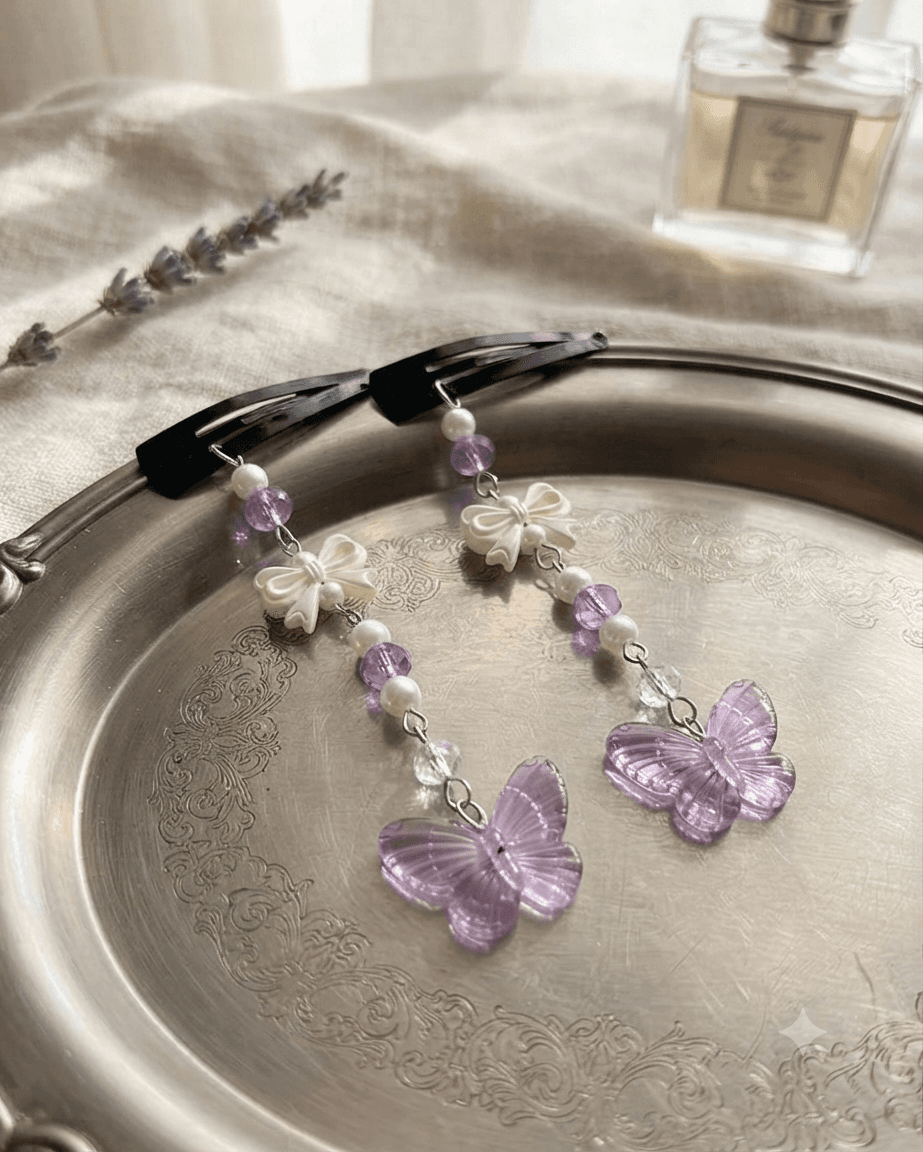 Pair of handmade purple butterfly hair clips with white bows and long beaded dangles displayed on a decorative tray.
