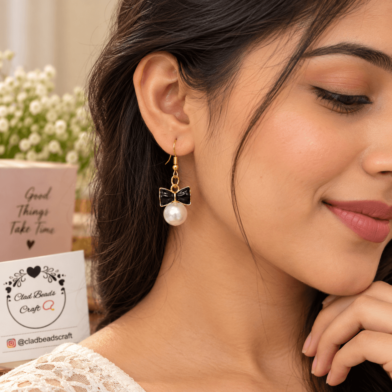 Woman wearing a black bow drop earring with a white pearl-look bead and gold-toned details.