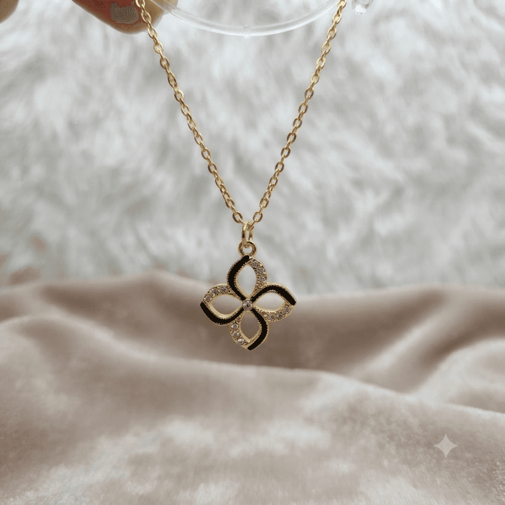 Black four-petal flower pendant necklace with a delicate gold-tone chain displayed against soft neutral fabric.