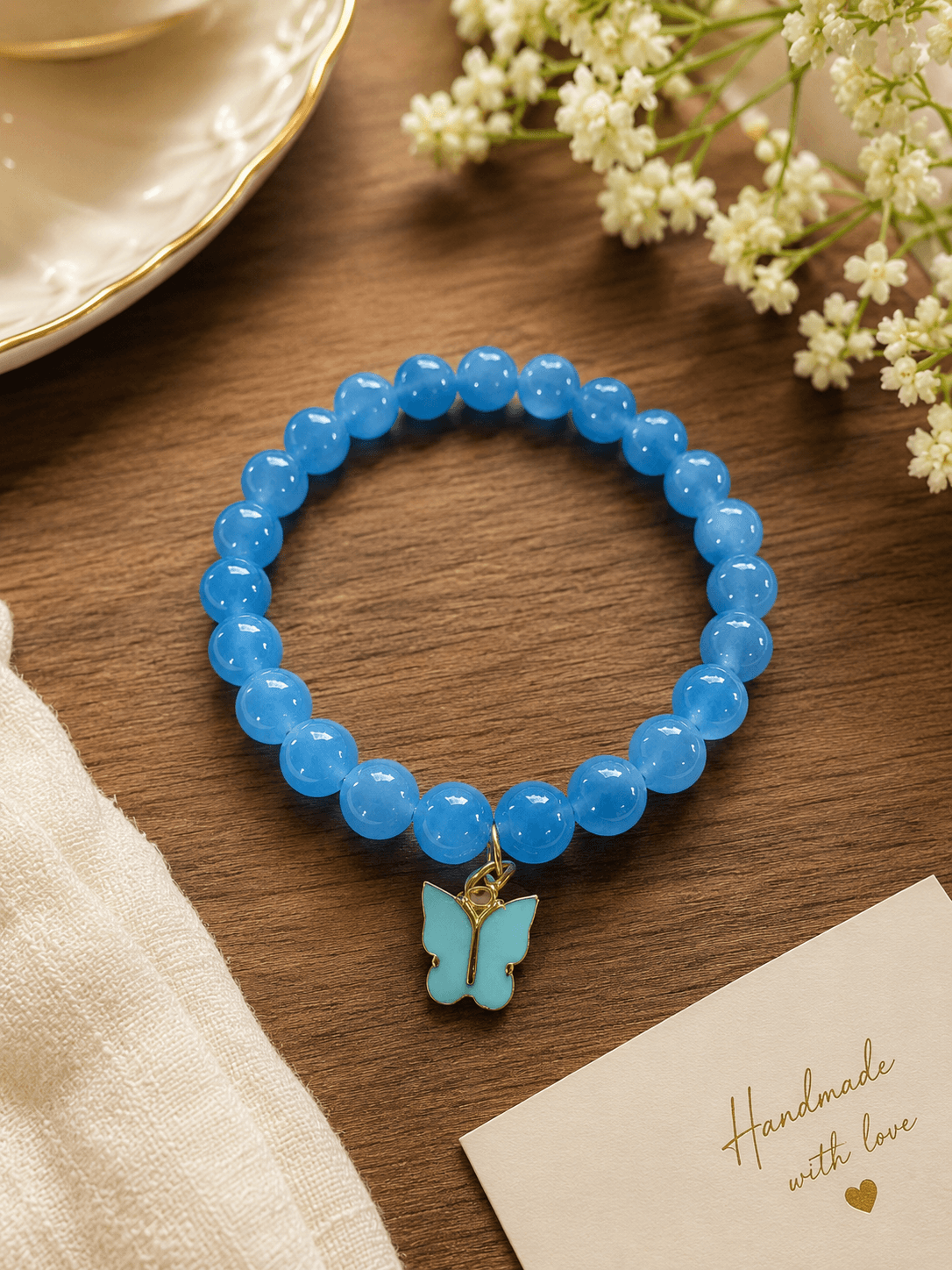 Handmade glossy blue beaded stretch bracelet with a blue butterfly charm in a gold-tone outline.