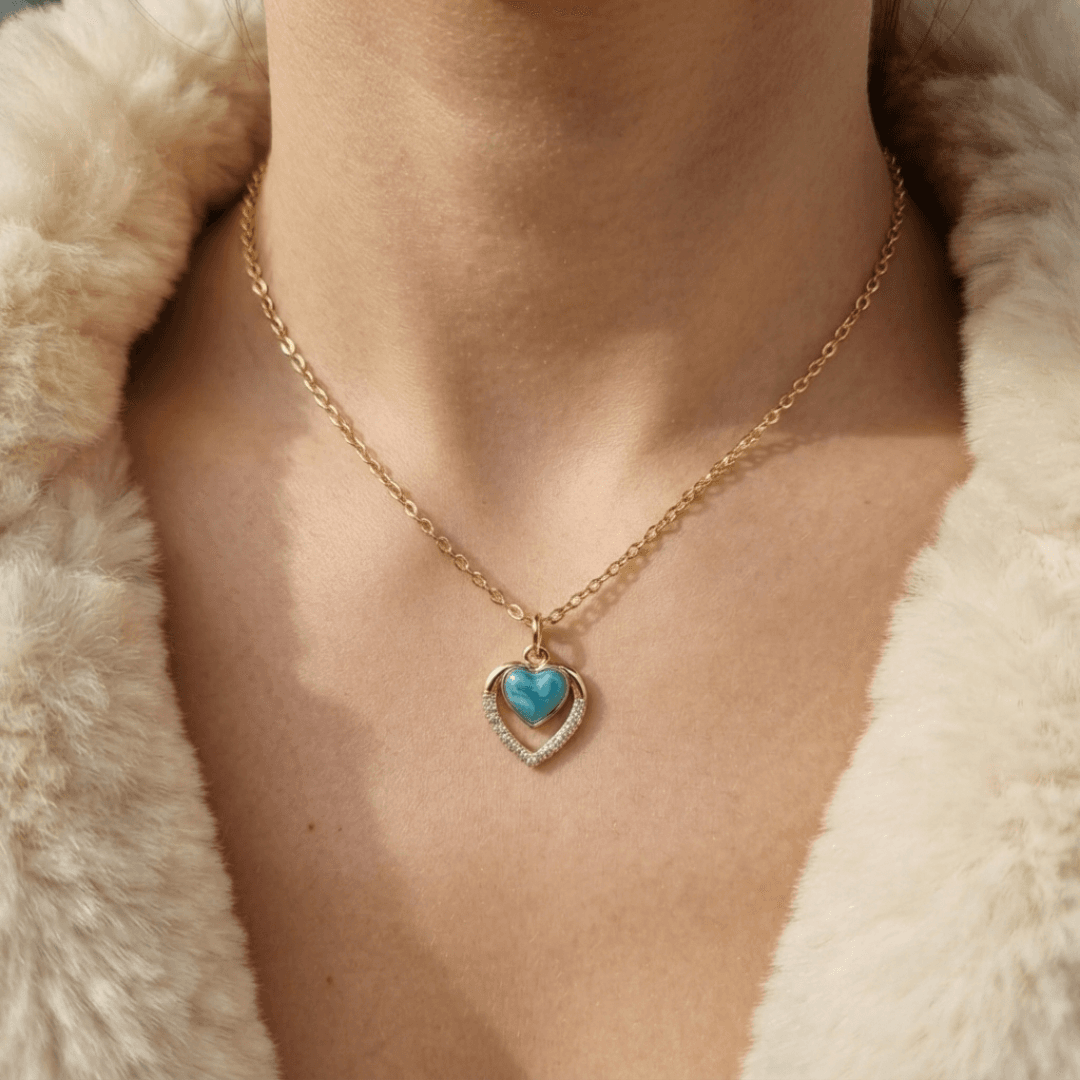 Blue heart pendant necklace with a gold-tone chain worn against a neutral outfit.