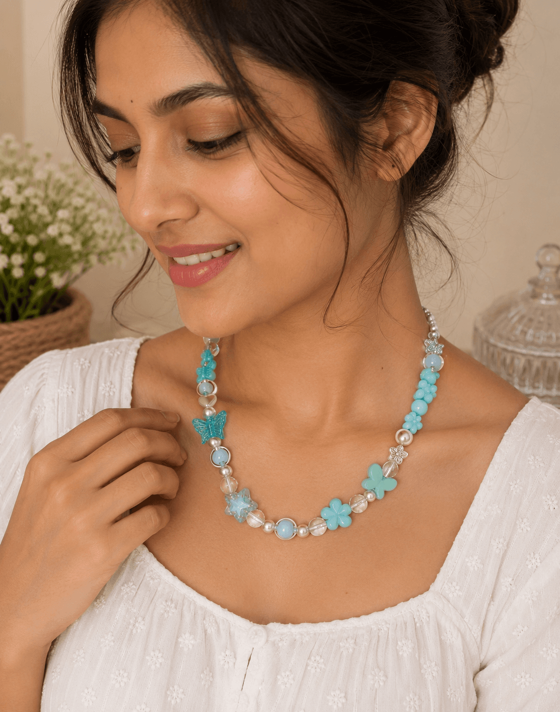 Woman wearing an aqua blue beaded necklace with butterfly and flower beads over a white embroidered outfit.