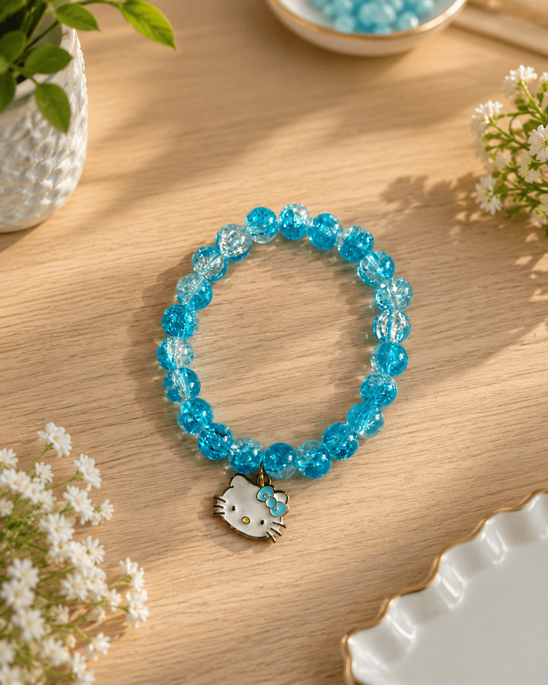 Blue beaded kitty charm bracelet with bright blue and clear beads displayed on a wooden surface with small white flowers.