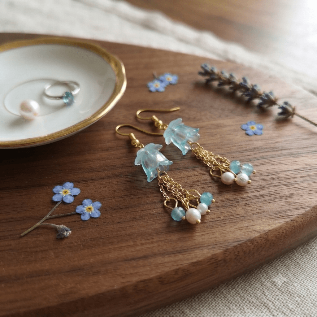 Pair of handmade aqua blue floral tassel earrings with translucent flower beads, gold-tone chain details and blue-white bead clusters displayed on a wooden surface.