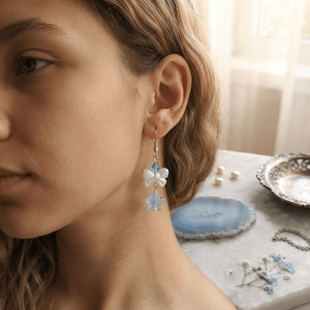 Woman wearing a handmade blue and white floral dangle earring with a translucent aqua star-shaped drop and silver-tone hook.