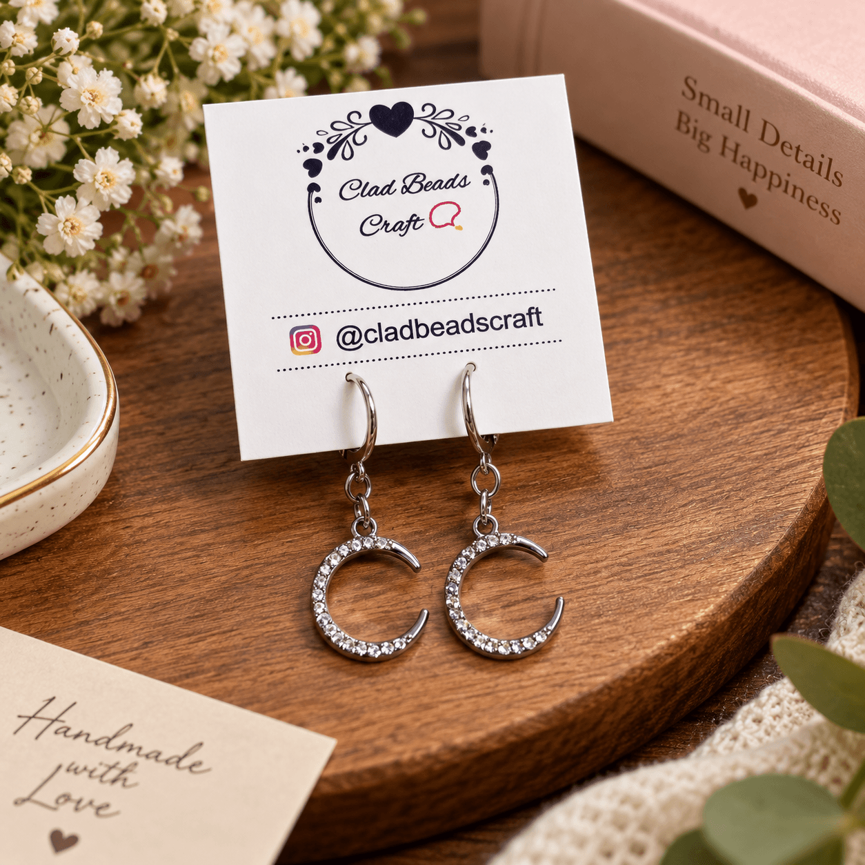 Pair of silver-tone crescent rhinestone hoop earrings displayed on Clad Beads Craft jewellery card