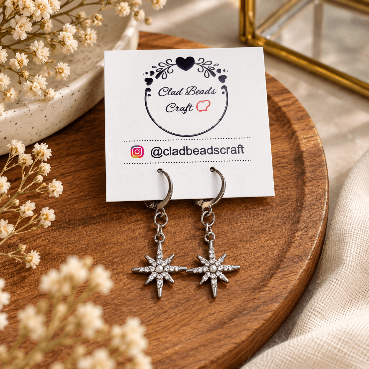 Pair of handmade silver-tone celestial star drop earrings with white pearl-look centres displayed on a Clad Beads Craft jewellery card.