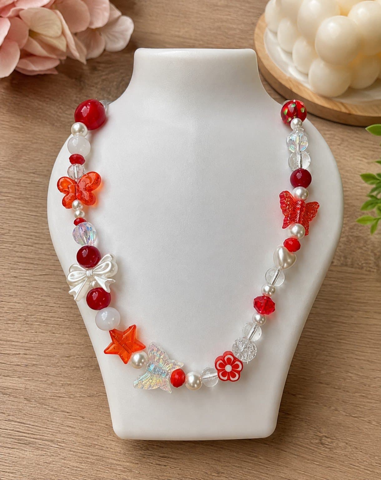 Red and white handmade beaded necklace with orange and red butterfly details, a white bow, star, flower and clear decorative beads.