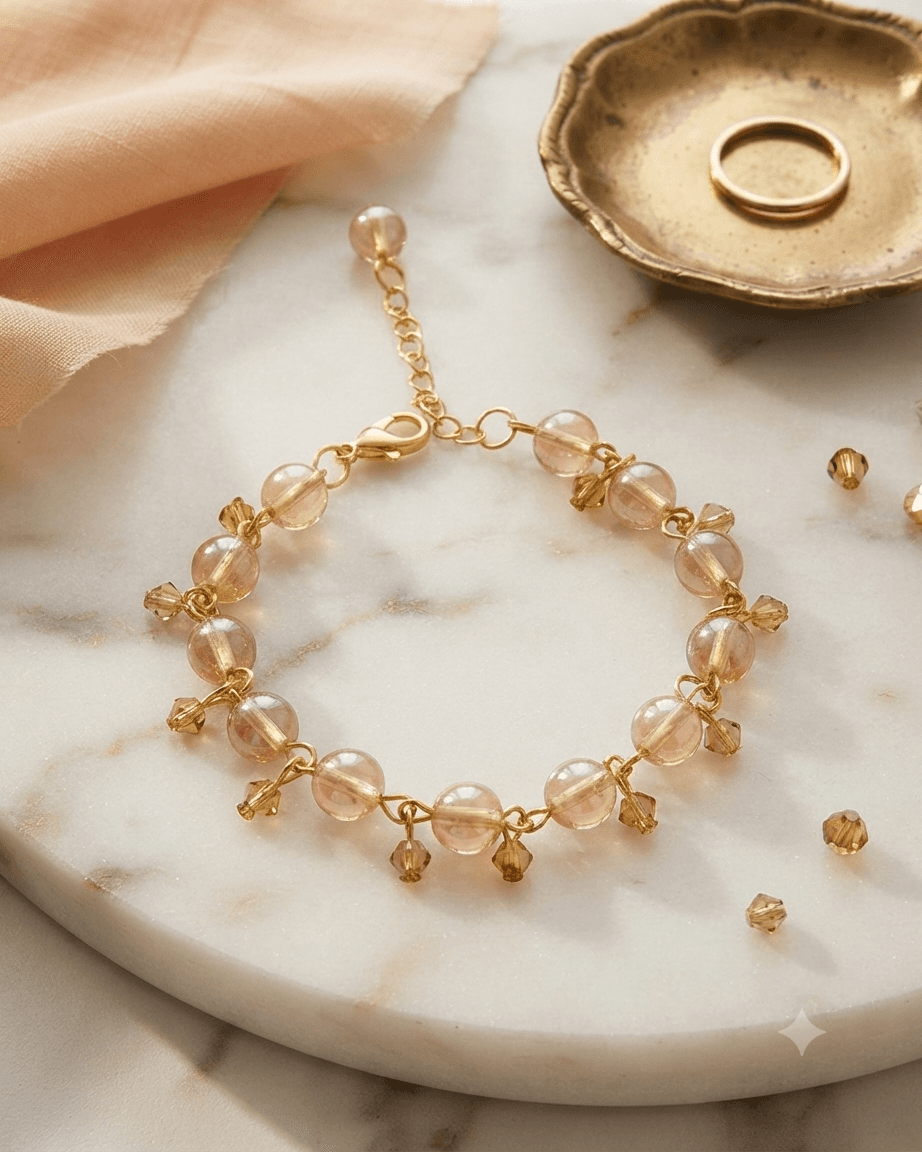 Champagne beaded bracelet with gold-tone chain details and dangling beads displayed on a white marble-style surface.