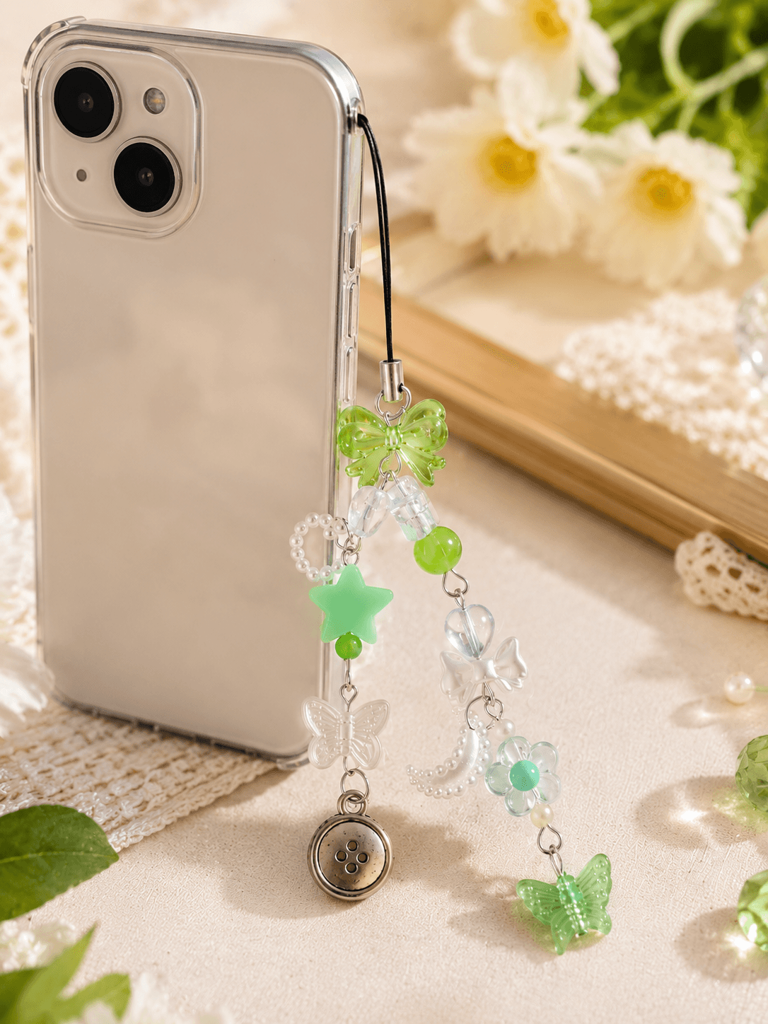 Clear phone case decorated with a handmade green beaded phone strap featuring a translucent green bow, star, butterflies, floral details and a round button charm.