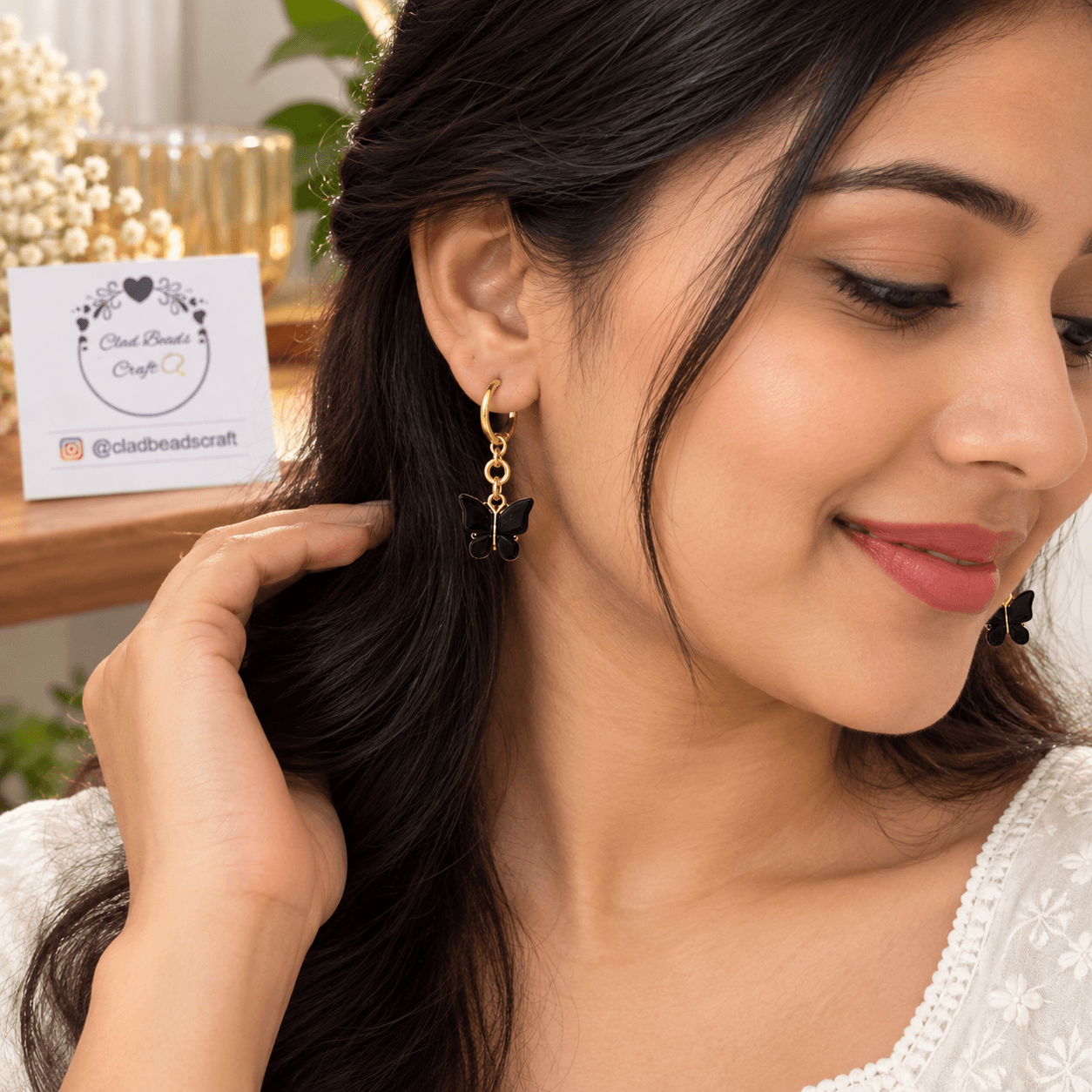 Woman wearing a black butterfly drop hoop earring with a gold-toned hoop and chain detail.
