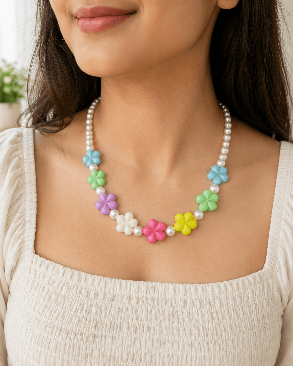 Woman wearing a handmade pastel flower bead necklace with colourful floral accents and pearl-look artificial beads over a white outfit.