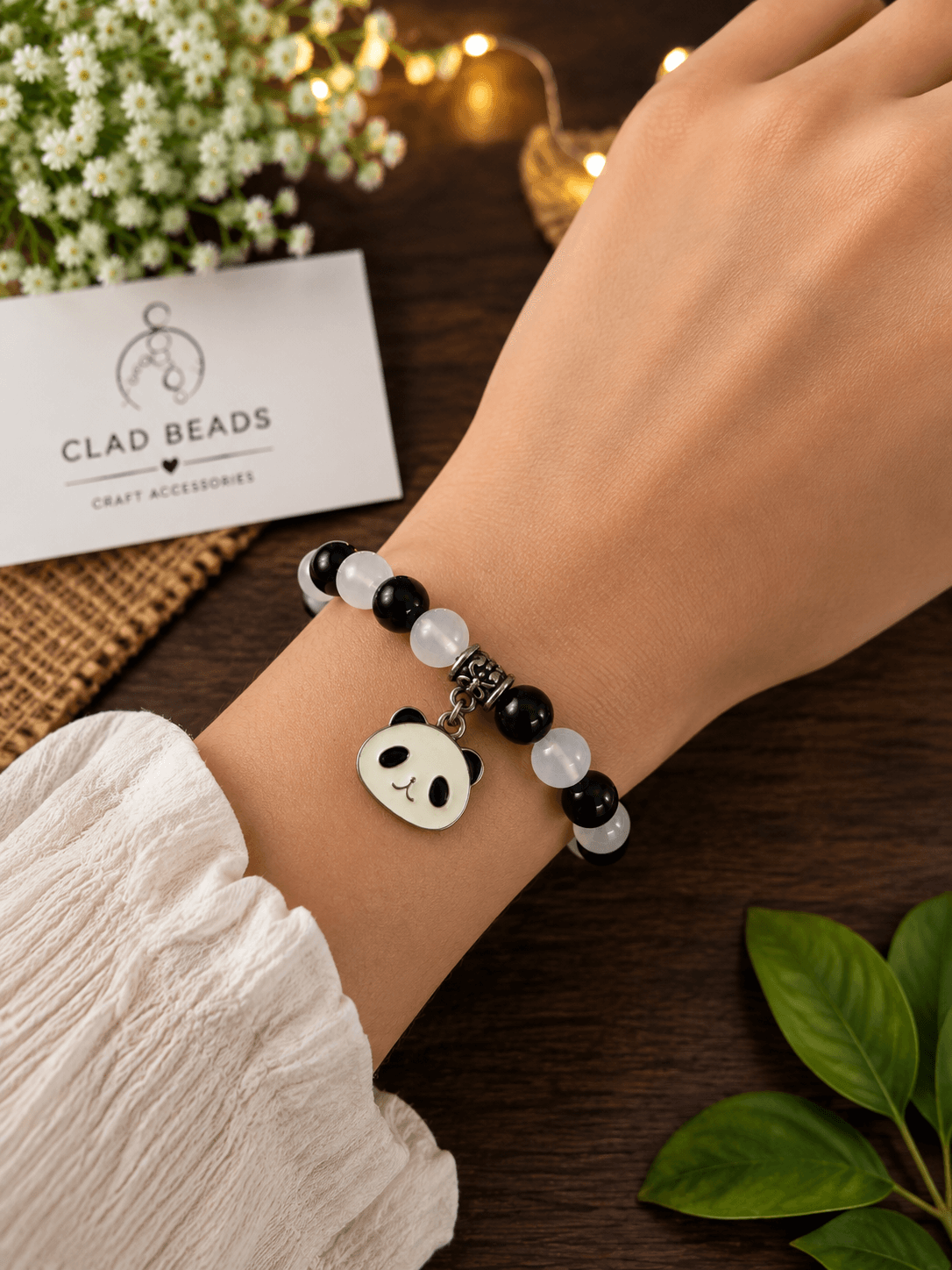 Black and white panda charm bracelet worn on a wrist with alternating round beads and a dangling panda face charm.