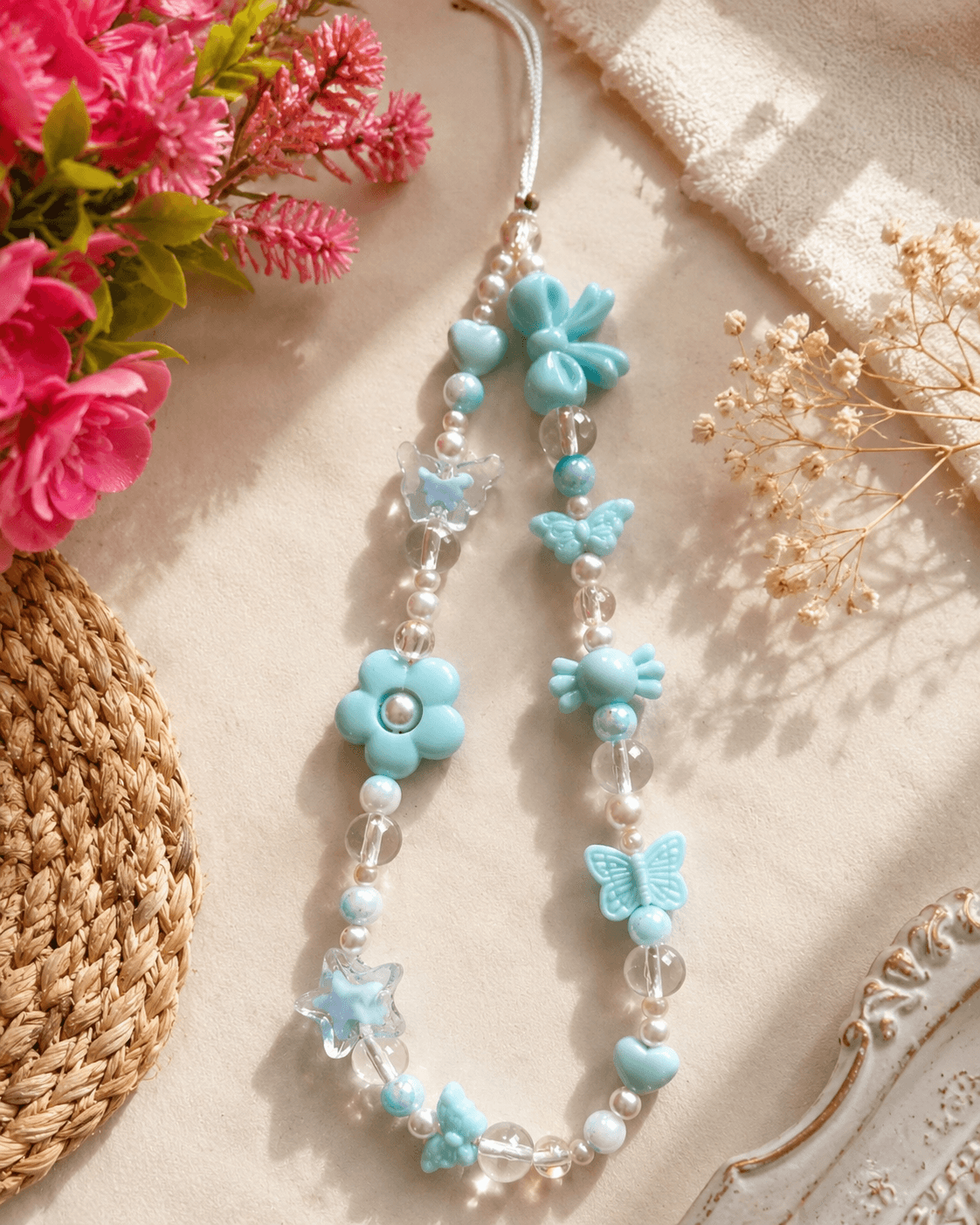Handmade pastel blue and mint beaded phone strap displayed with clear beads, white pearl-look accents, butterflies, flowers, hearts and star-shaped details.