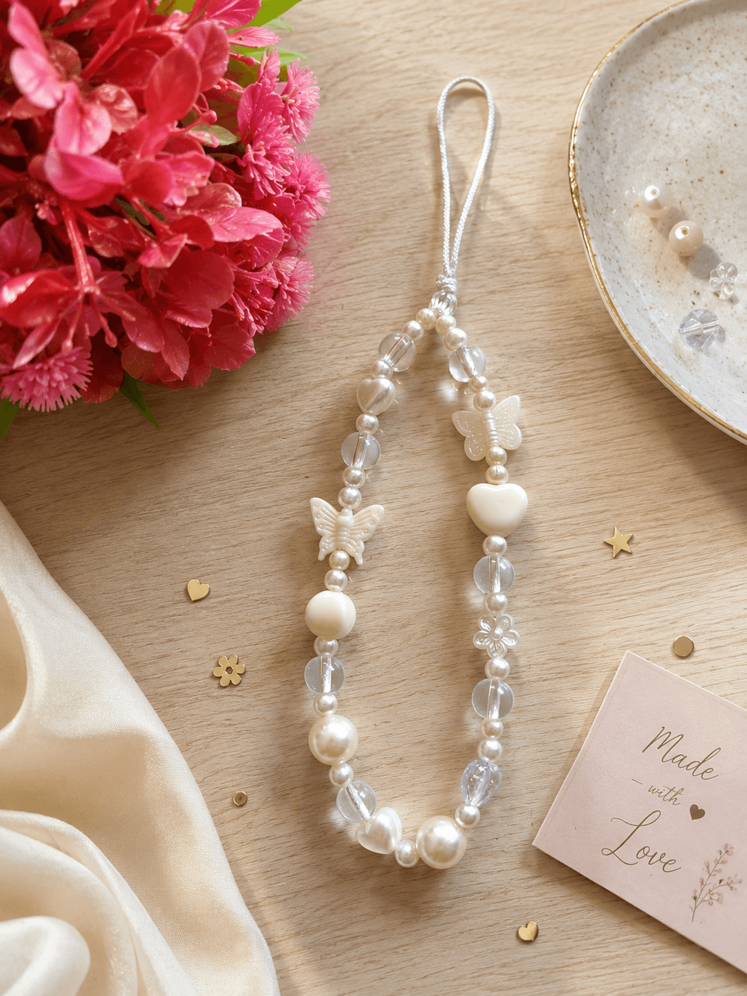 Handmade white pearl-look phone strap with butterfly, heart, flower and clear acrylic bead details on a white nylon loop.