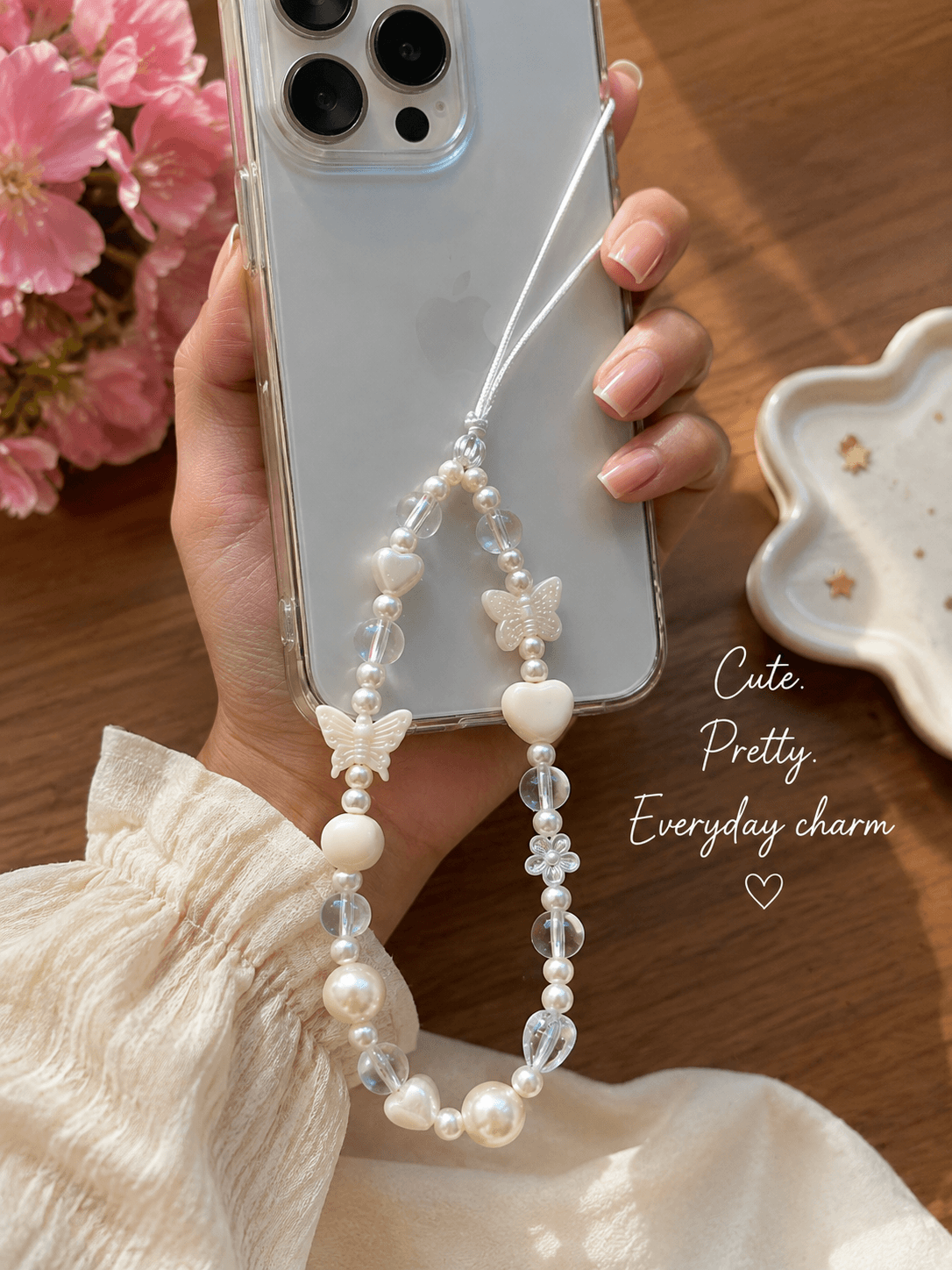 White pearl-look butterfly phone strap attached to a clear phone case and held in hand.