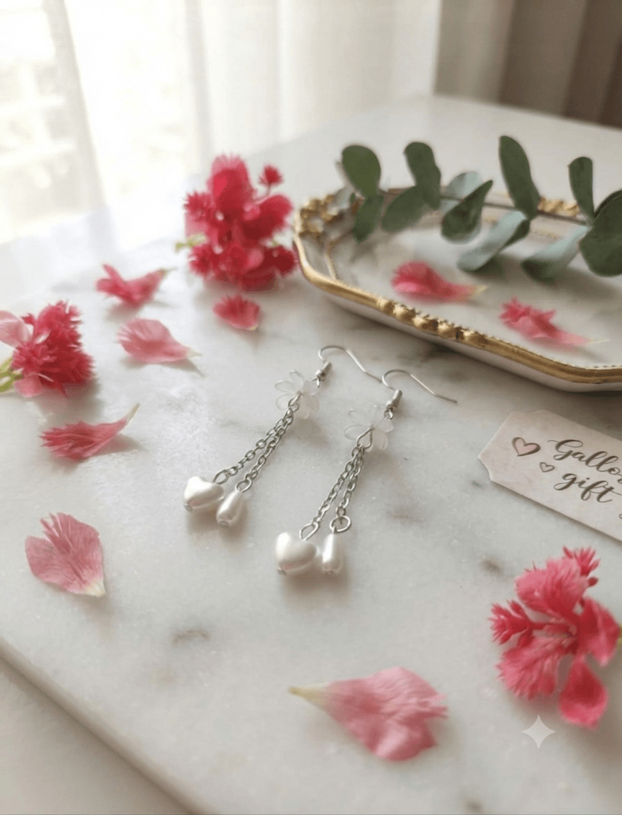 Pair of white floral heart drop earrings displayed on a soft white surface with pink flowers