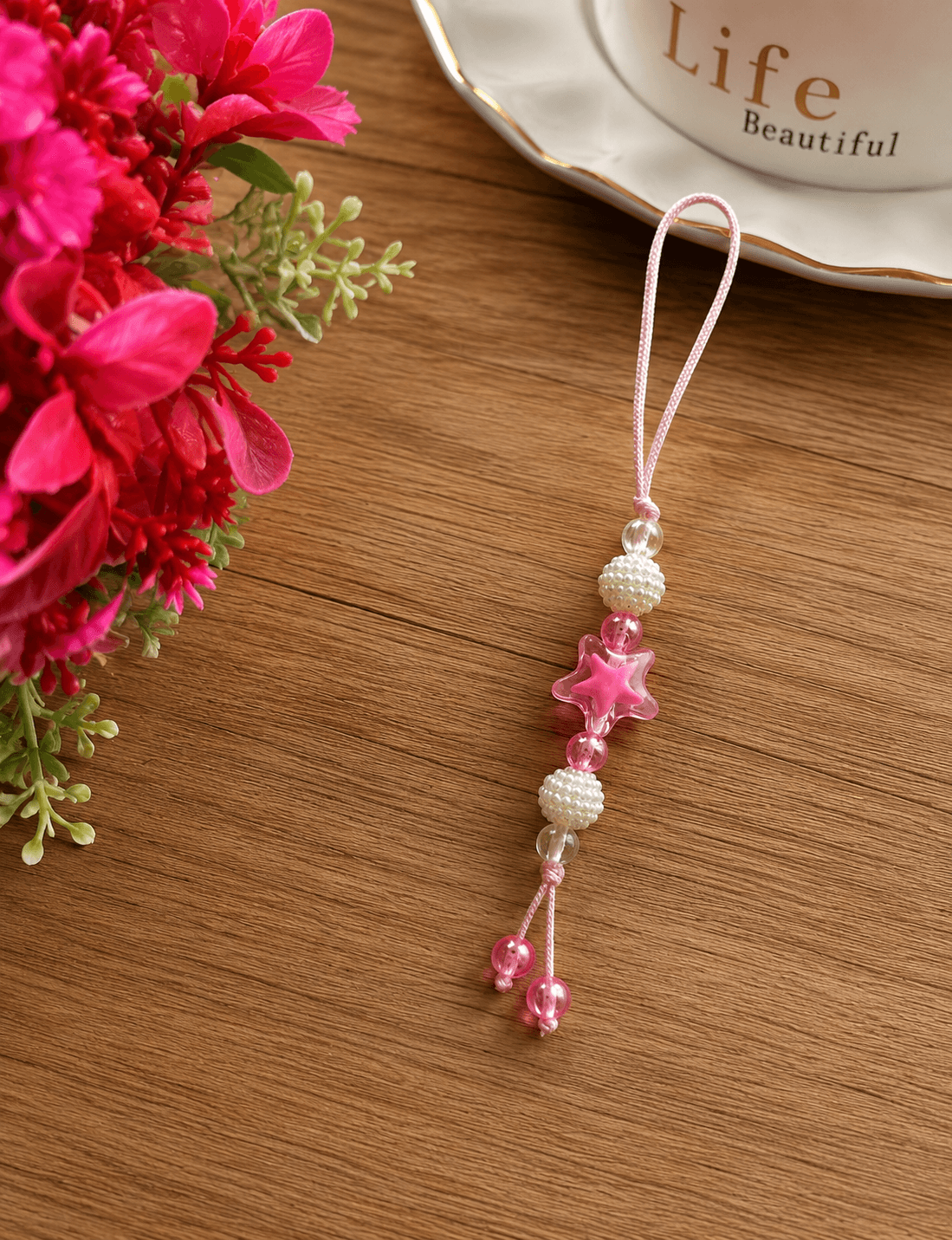 Pink and white handmade beaded phone strap displayed on a wooden surface with a translucent pink star charm and pearl-look beads.
