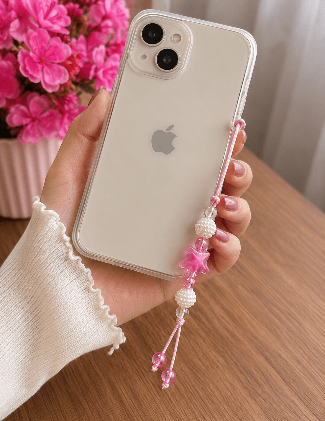 : Pink handmade phone strap attached to a clear phone case, featuring a translucent pink star and white pearl-look beads.