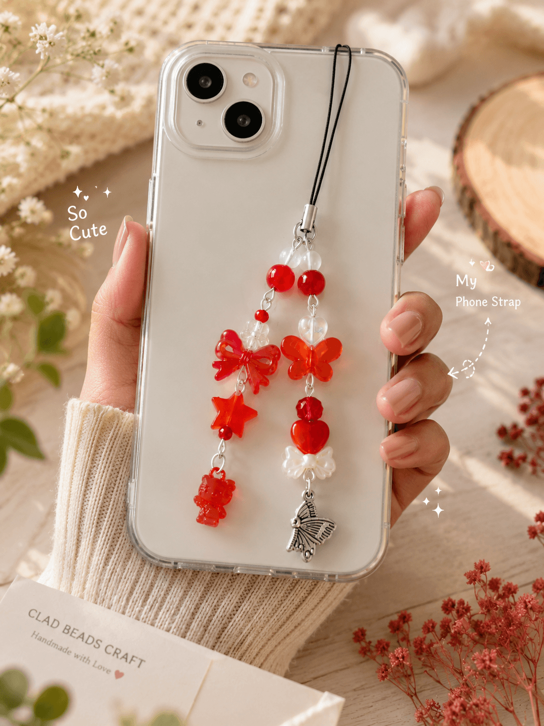 Clear phone case with a handmade red and orange beaded phone charm strap featuring bows, butterflies, hearts, stars, teddy bear and pearl-look details.