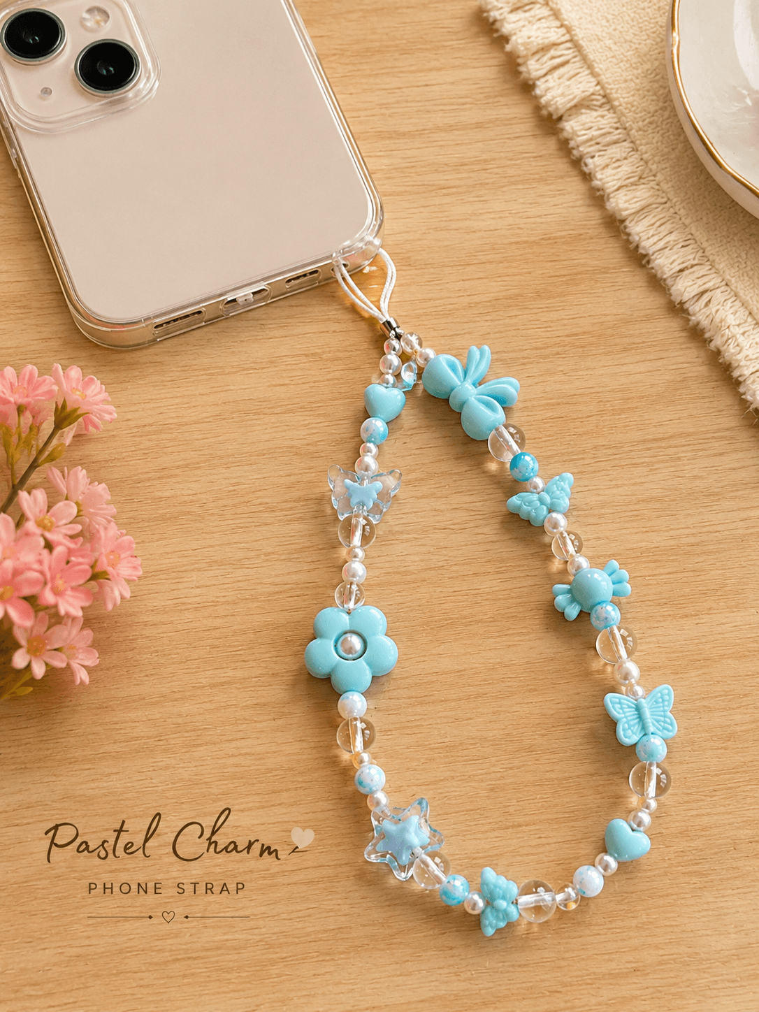 Clear smartphone case styled with a handmade pastel blue beaded phone strap featuring butterflies, flowers, hearts, stars and pearl-look accents.