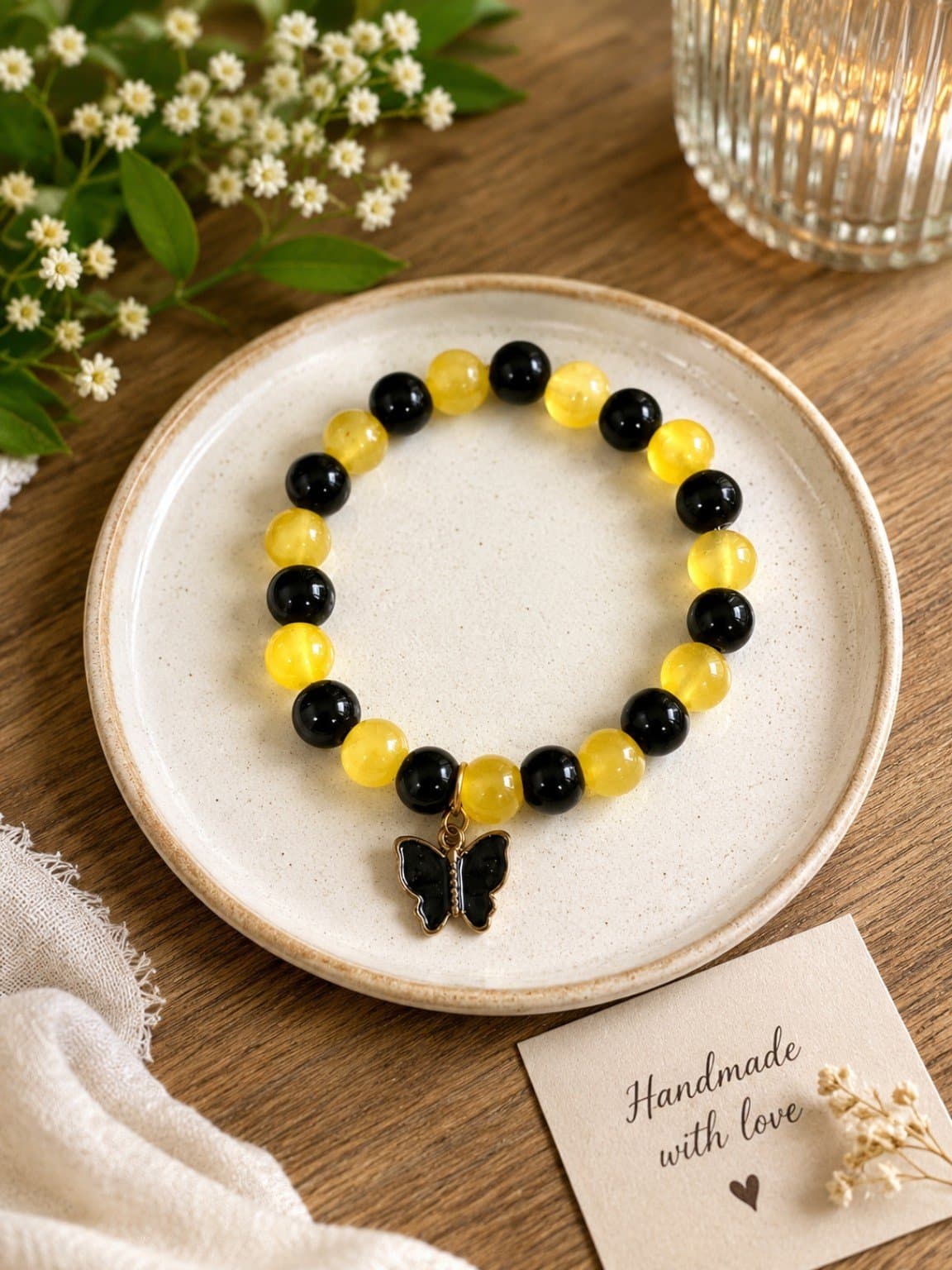 Black and yellow beaded butterfly bracelet displayed on a cream ceramic plate with a dangling butterfly charm.
