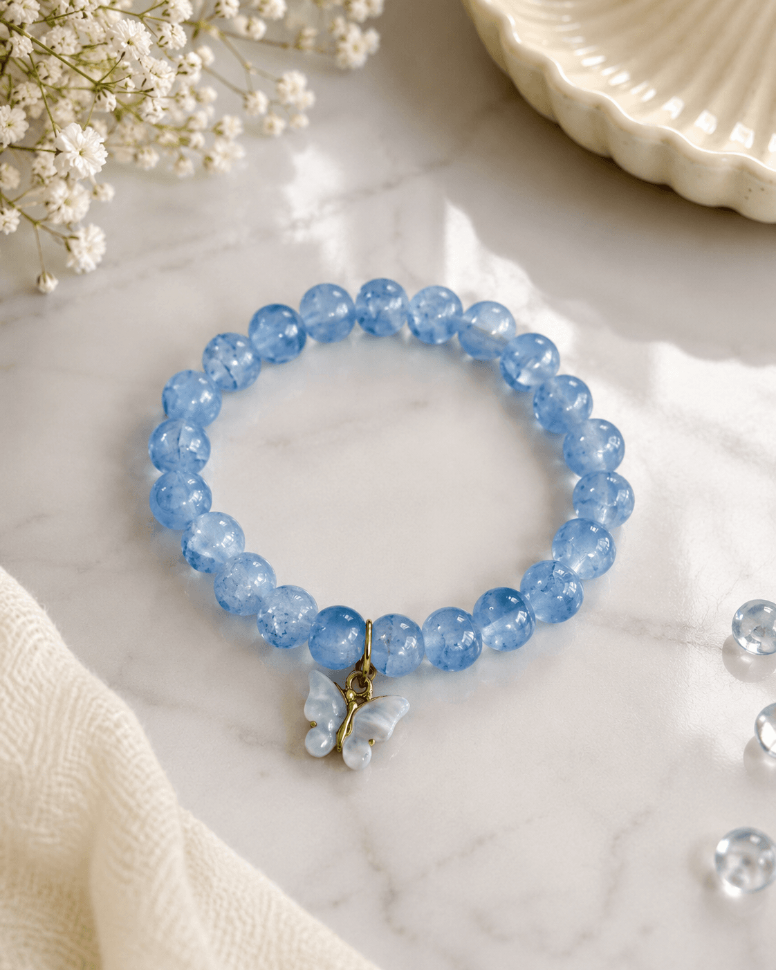 Handmade translucent blue crack-effect beaded bracelet with a pale blue butterfly charm and gold-tone finding.