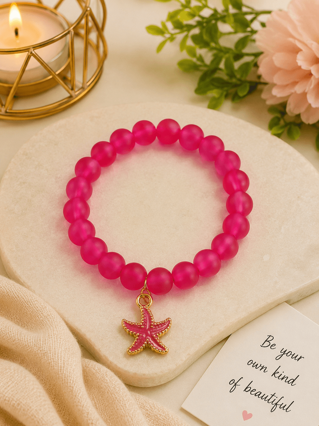 Hot pink beaded bracelet with a starfish charm displayed on a cream decorative surface.