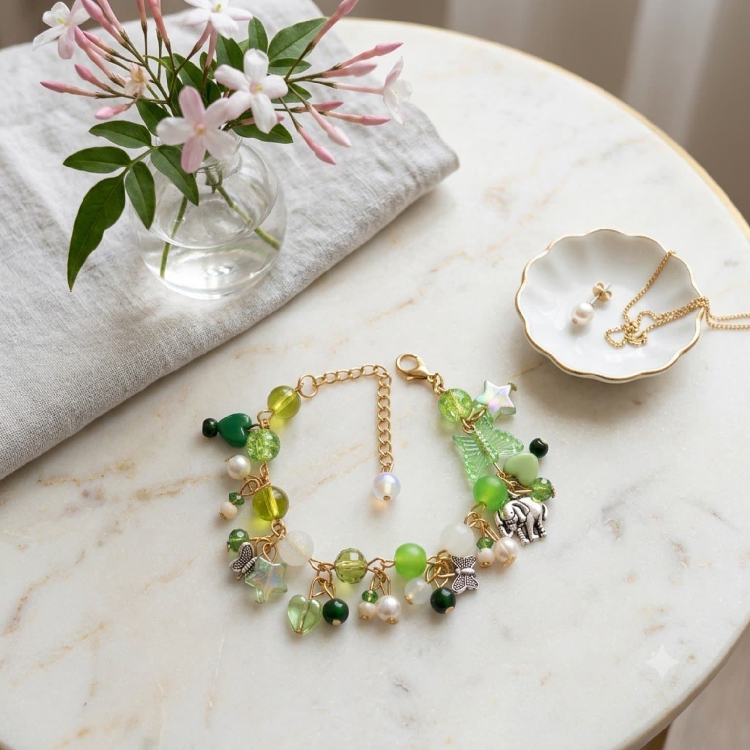 Handmade green beaded chain bracelet with butterfly, star, heart, leaf and elephant-inspired charms on a light surface.