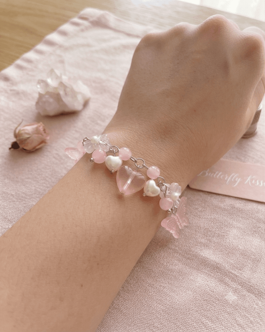 Pink and white handmade beaded bracelet worn on a wrist with butterfly, heart and flower details.