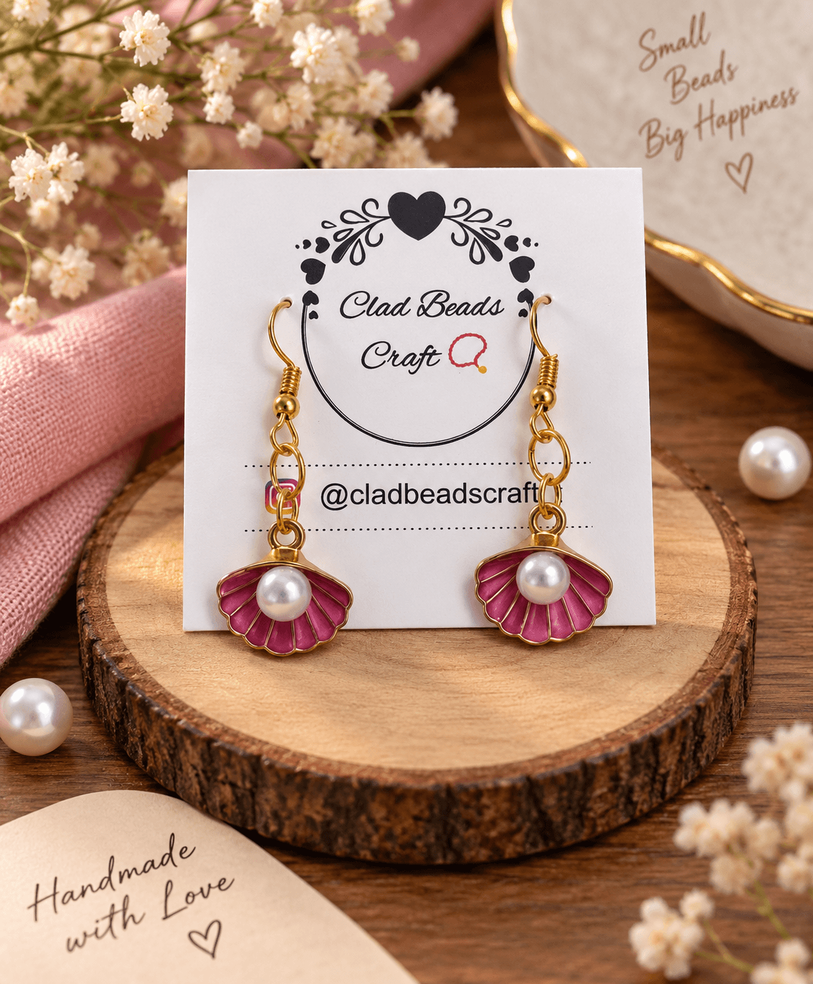 Pair of pink scalloped floral drop earrings with white pearl-look centres and gold-tone hooks displayed on a jewellery card.