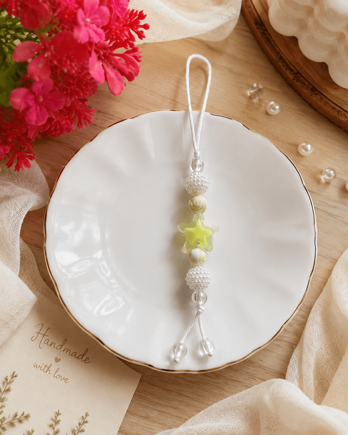 Handmade pastel yellow and white beaded phone strap with a translucent yellow star, rose-inspired bead, pearl-look ball beads and clear round beads displayed on a white dish.