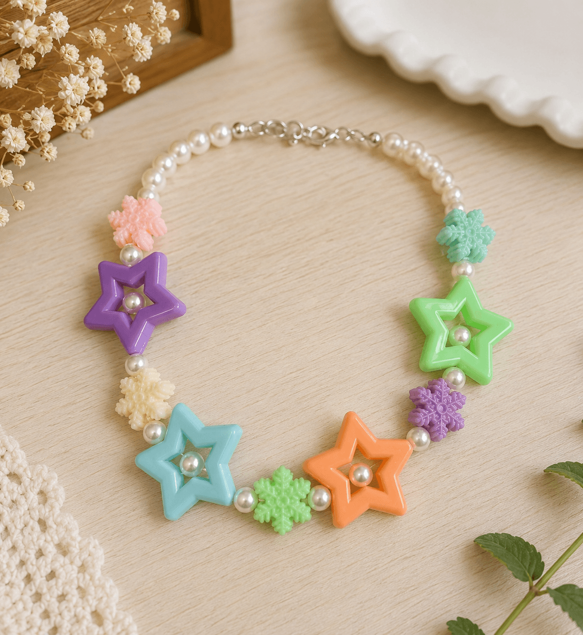 Multicolour star and snowflake acrylic bead necklace arranged on a light wooden surface with pearl-look round accents.