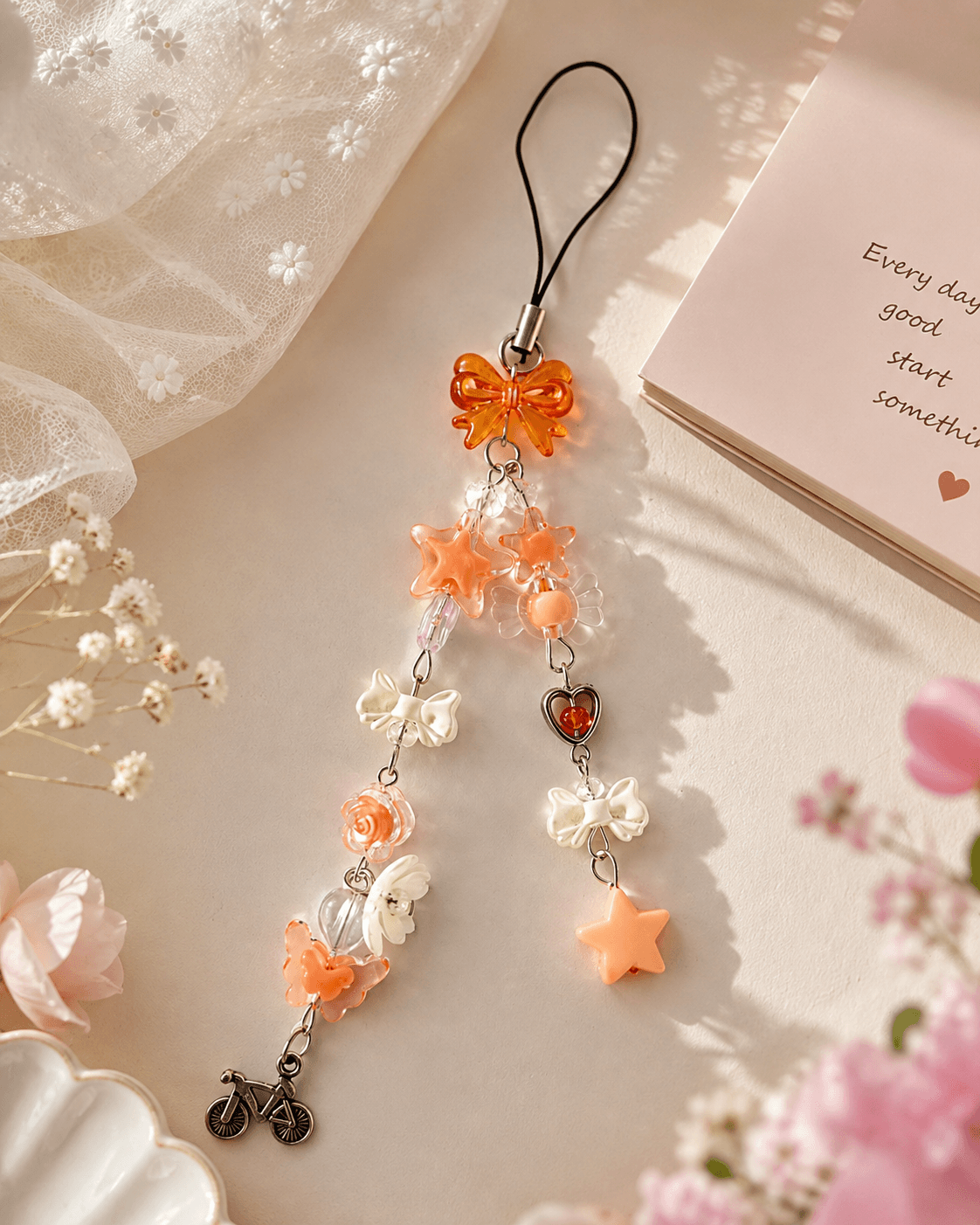 Handmade peach bow phone charm with floral, star, butterfly, heart and bicycle charms displayed on a soft neutral background.