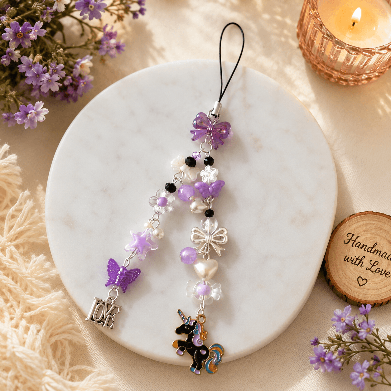 Handmade purple phone charm strap displayed with purple flowers, butterfly details, pearl-look beads, star, LOVE and unicorn charms.