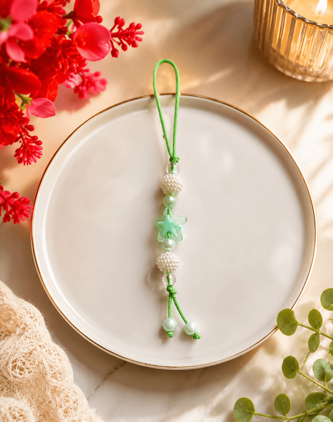 Mint-green beaded phone strap with a star-shaped bead, white textured beads and green cord displayed on a ceramic plate.