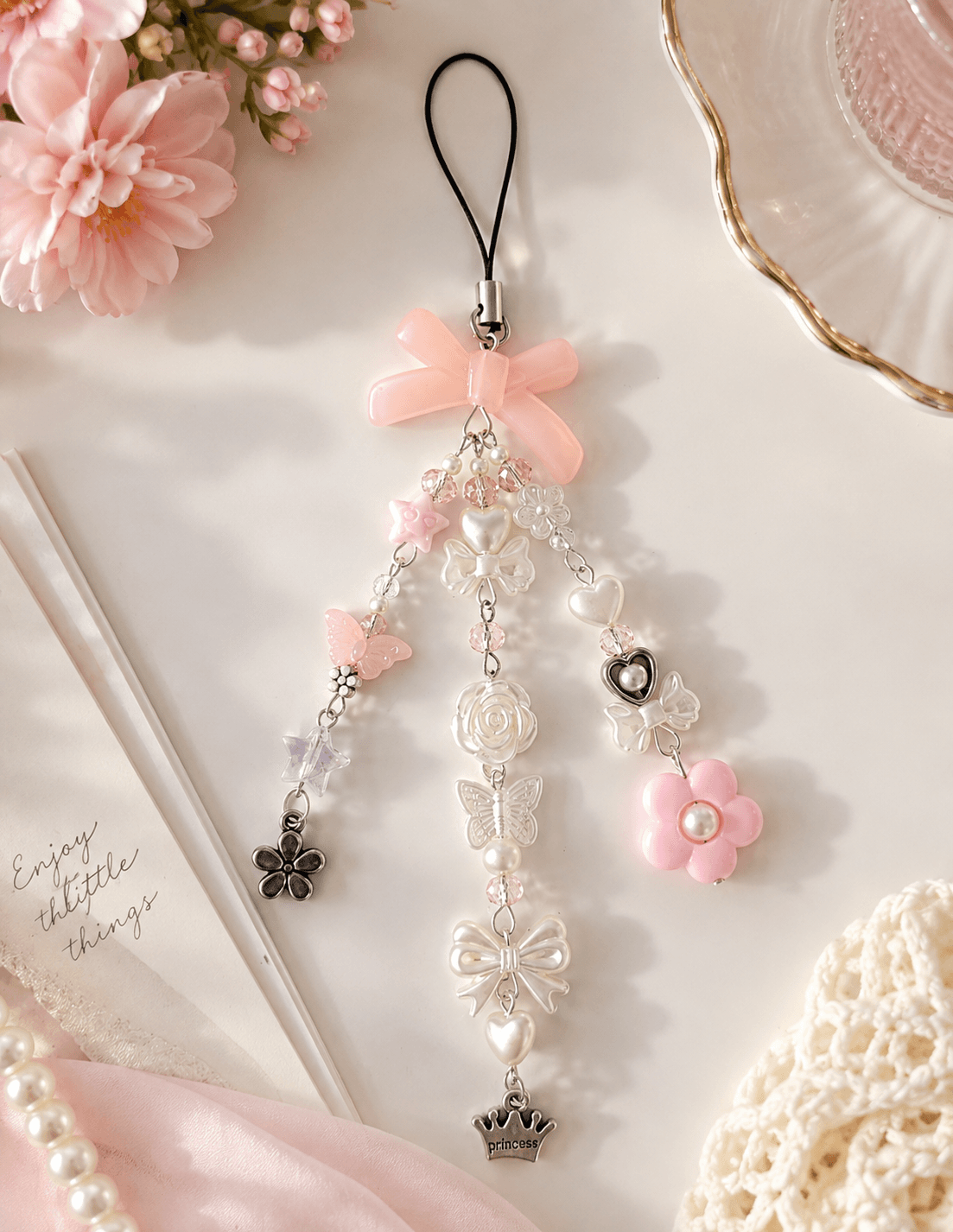 Handmade pastel pink and white beaded phone charm displayed with bows, hearts, butterflies, flowers, stars and a princess crown charm.